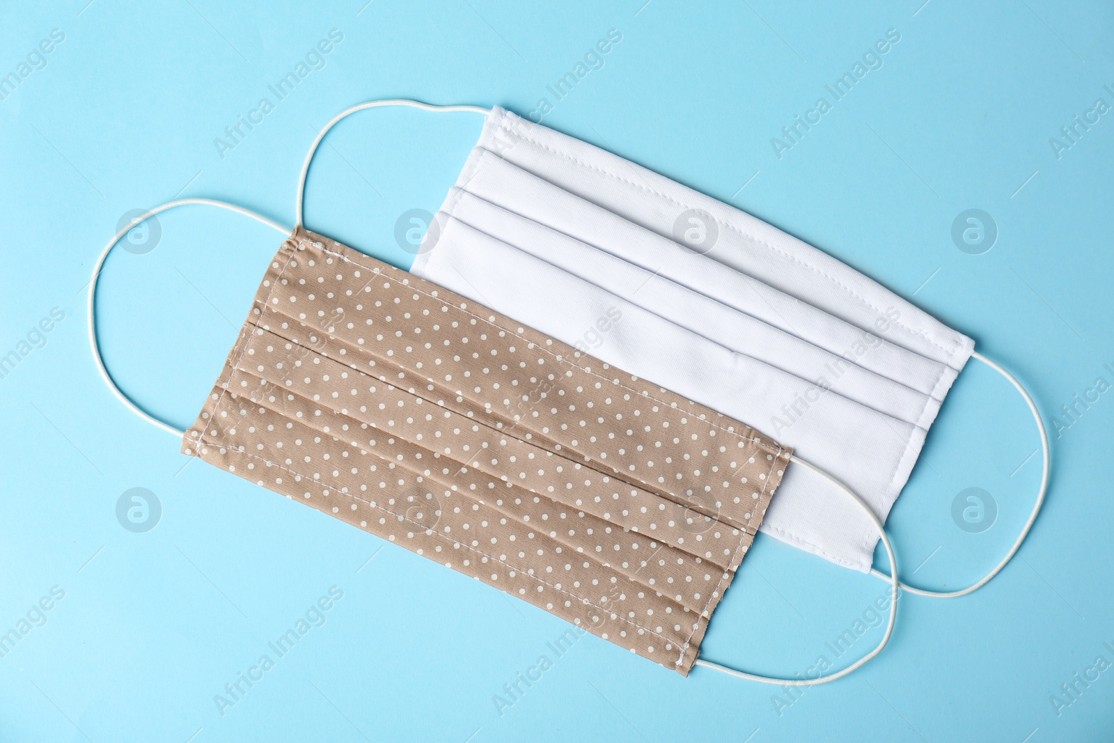 Photo of Homemade protective face masks on light blue background, flat lay