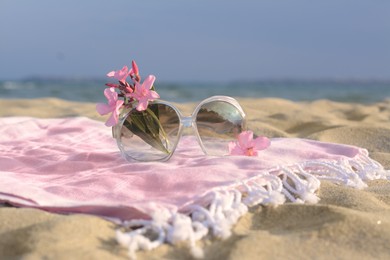 Beautiful sunglasses with tropical flower on blanket near sea