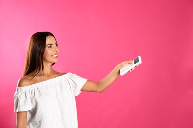 Young woman with air conditioner remote on pink background