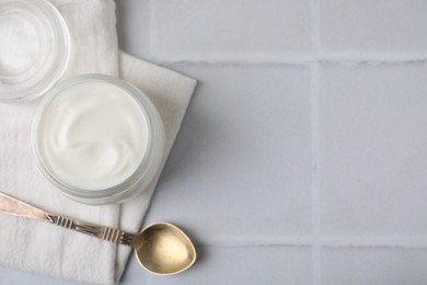 Delicious natural yogurt in jar and spoon on white tiled table, top view. Space for text