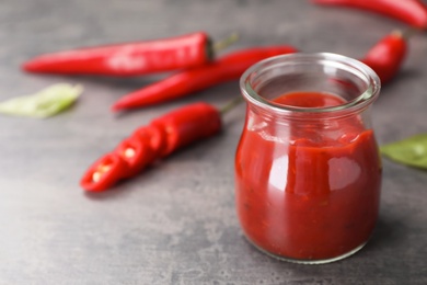 Jar with spicy chili sauce on dark table