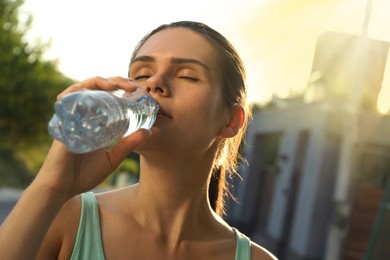 Photo of Young woman drinking water outdoors on hot summer day. Refreshing drink