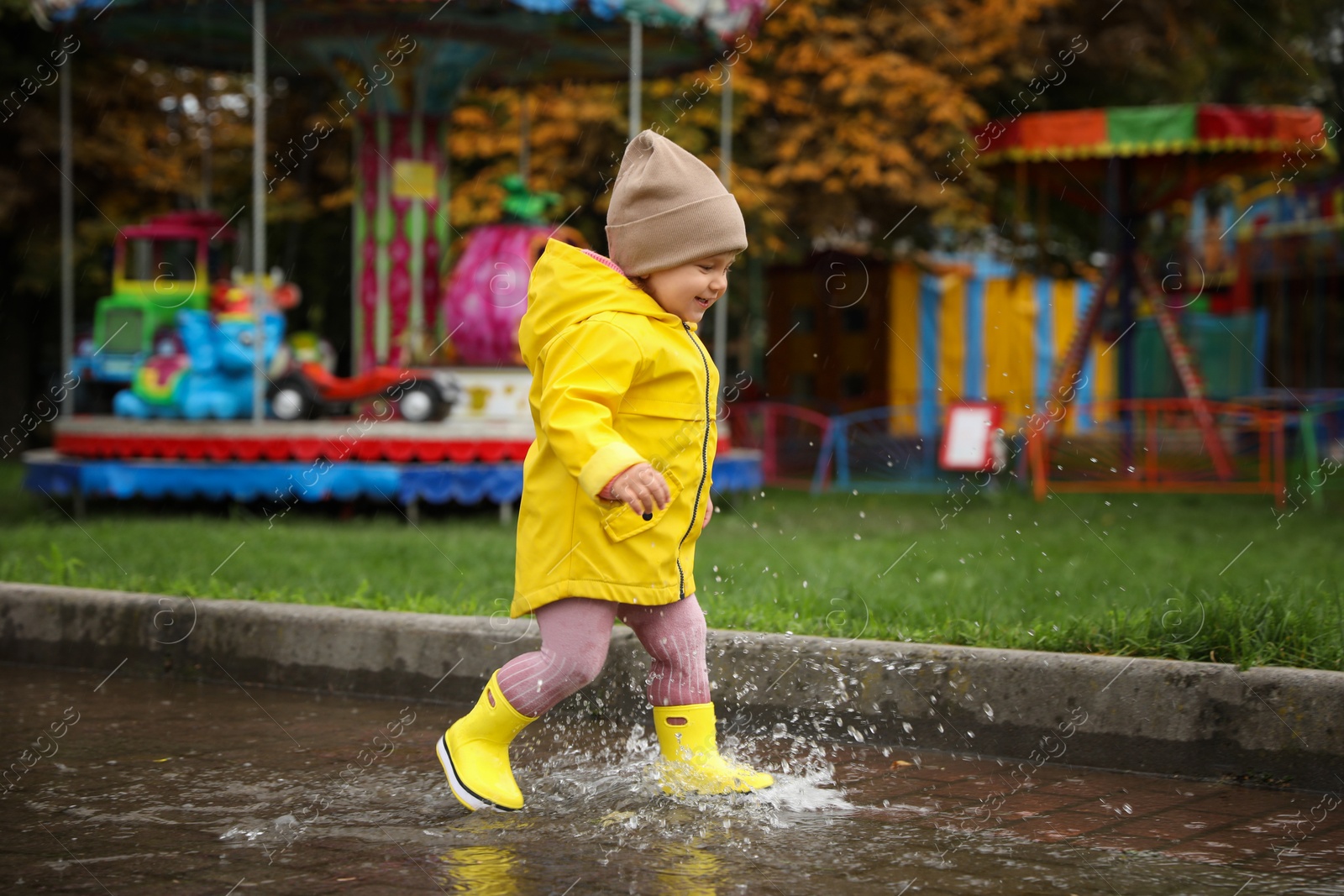 Photo of Cute little girl walking in puddle outdoors on rainy weather