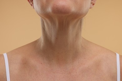 Woman showing her neck on beige background, closeup