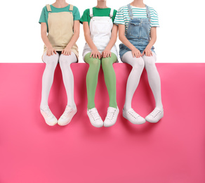 Group of women wearing colorful tights and stylish shoes sitting on color background, closeup