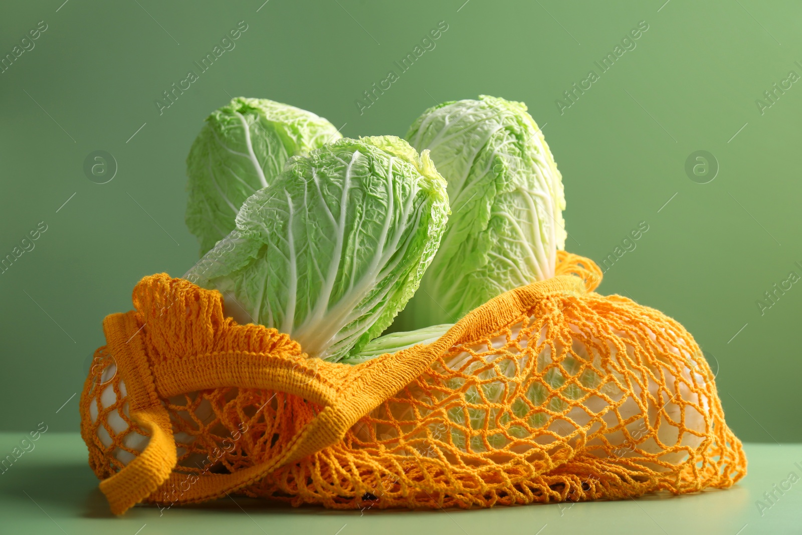 Photo of Fresh Chinese cabbages in string bag on green background, closeup