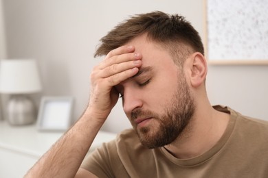 Photo of Young man suffering from migraine at home