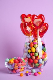 Photo of Delicious heart shaped lollipops and dragees on violet background