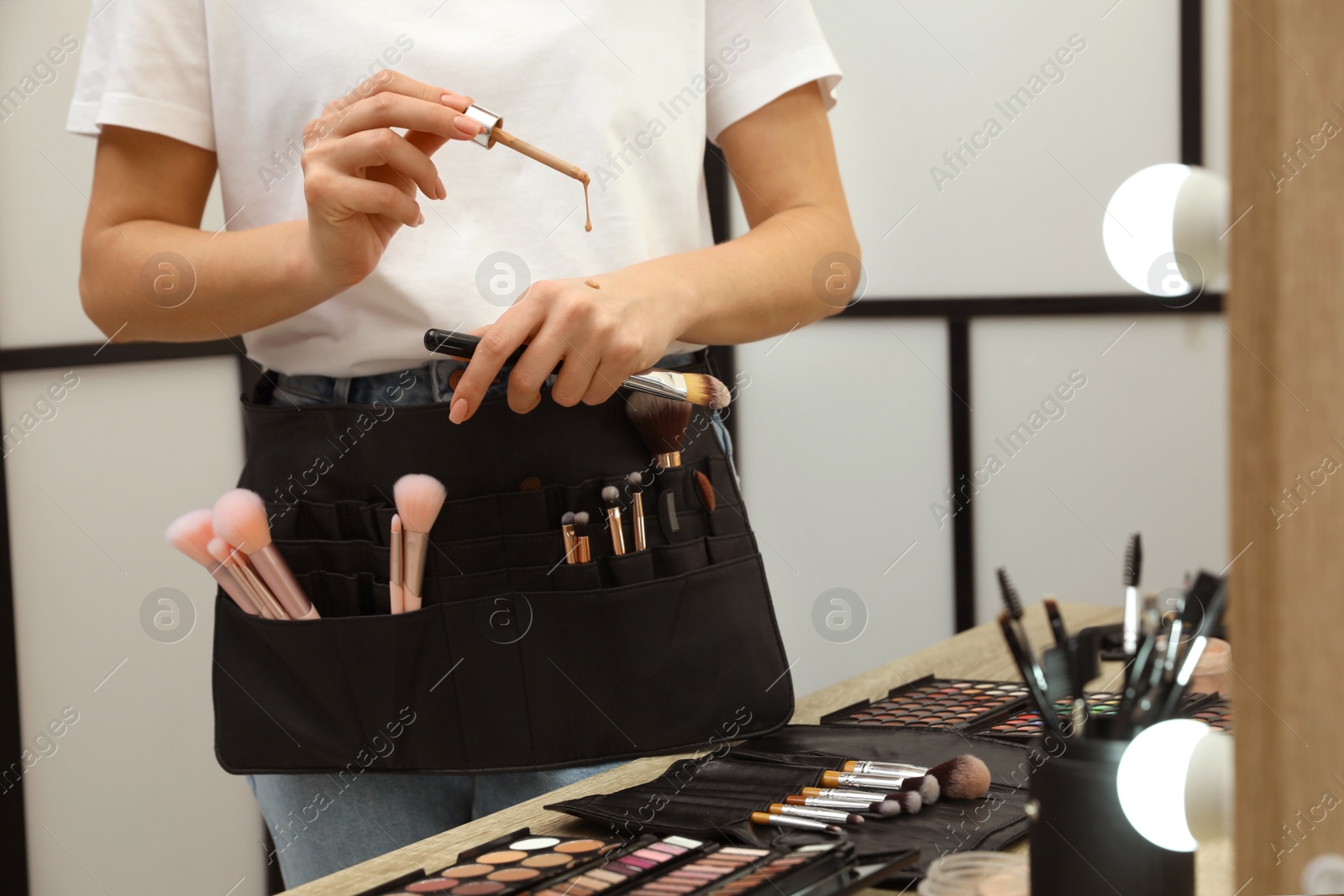 Photo of Professional makeup artist testing liquid foundation on hand near wooden table indoors, closeup