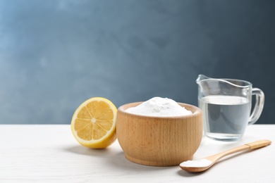 Photo of Baking soda, cut lemon and vinegar on white wooden table