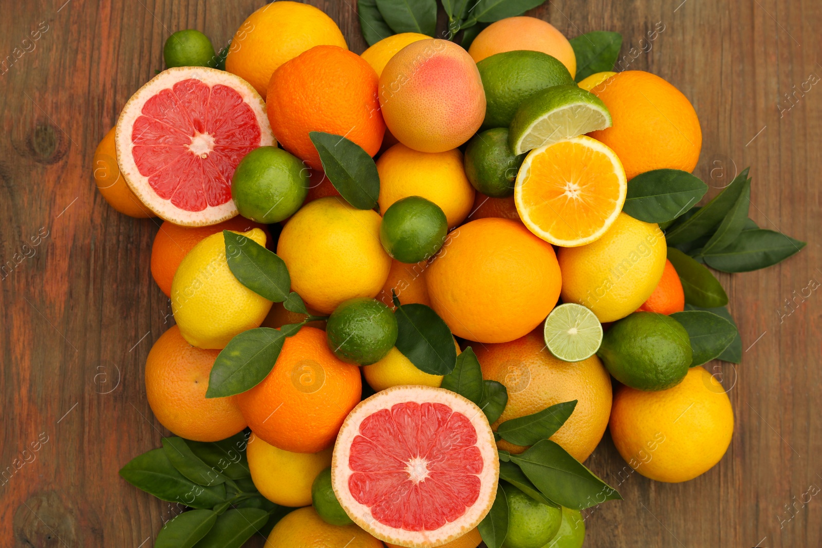 Photo of Different citrus fruits with green leaves on wooden table, flat lay