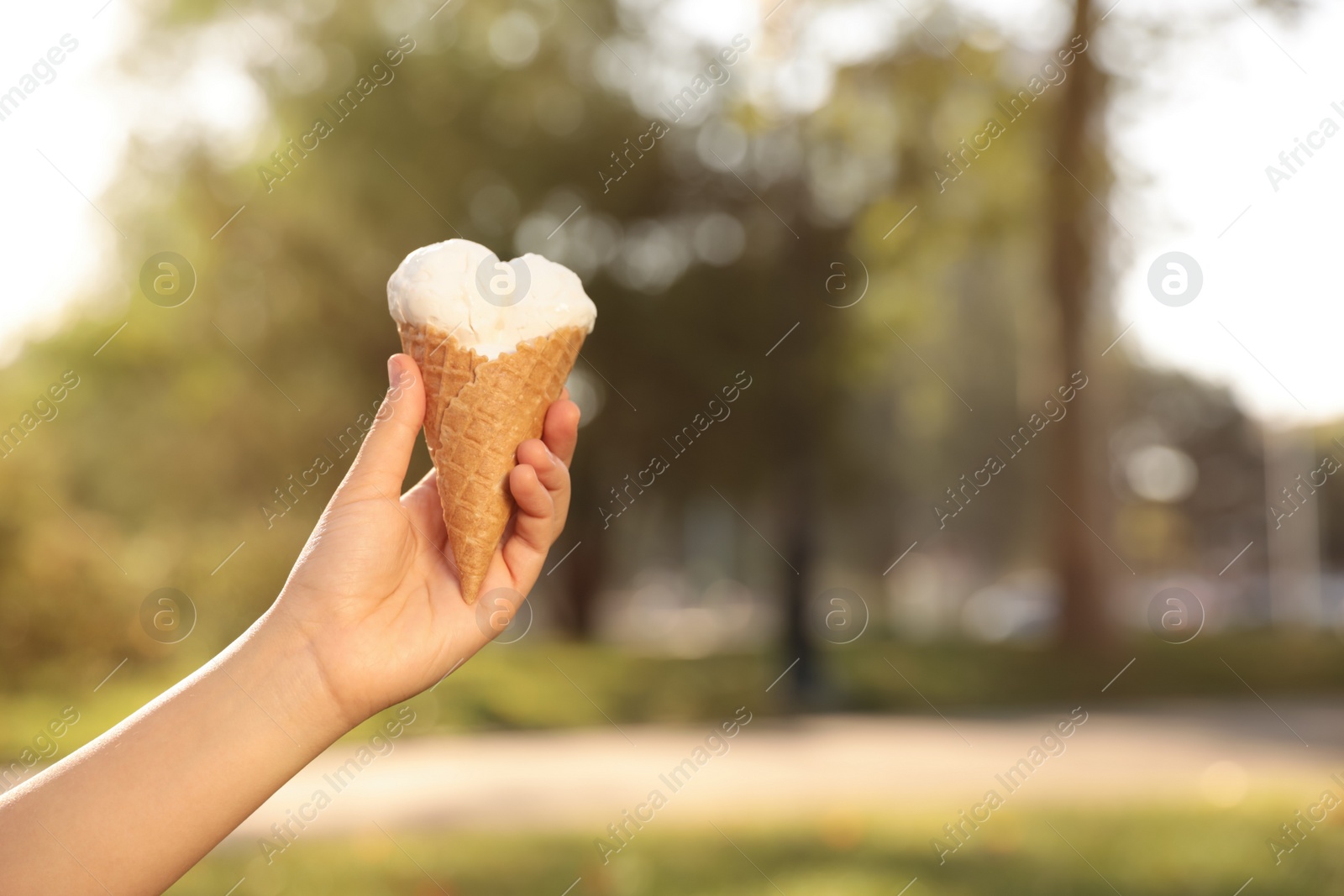 Photo of Woman holding delicious ice cream in waffle cone outdoors, closeup of hand. Space for text