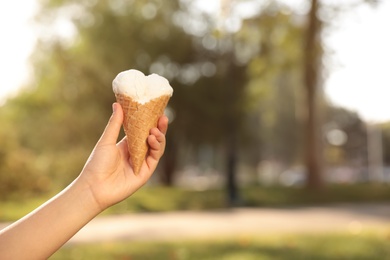Photo of Woman holding delicious ice cream in waffle cone outdoors, closeup of hand. Space for text