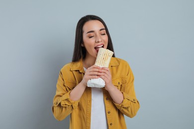 Photo of Young woman eating tasty shawarma on grey background