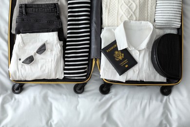 Photo of Open suitcase with clothes, passport and accessories on bed, top view