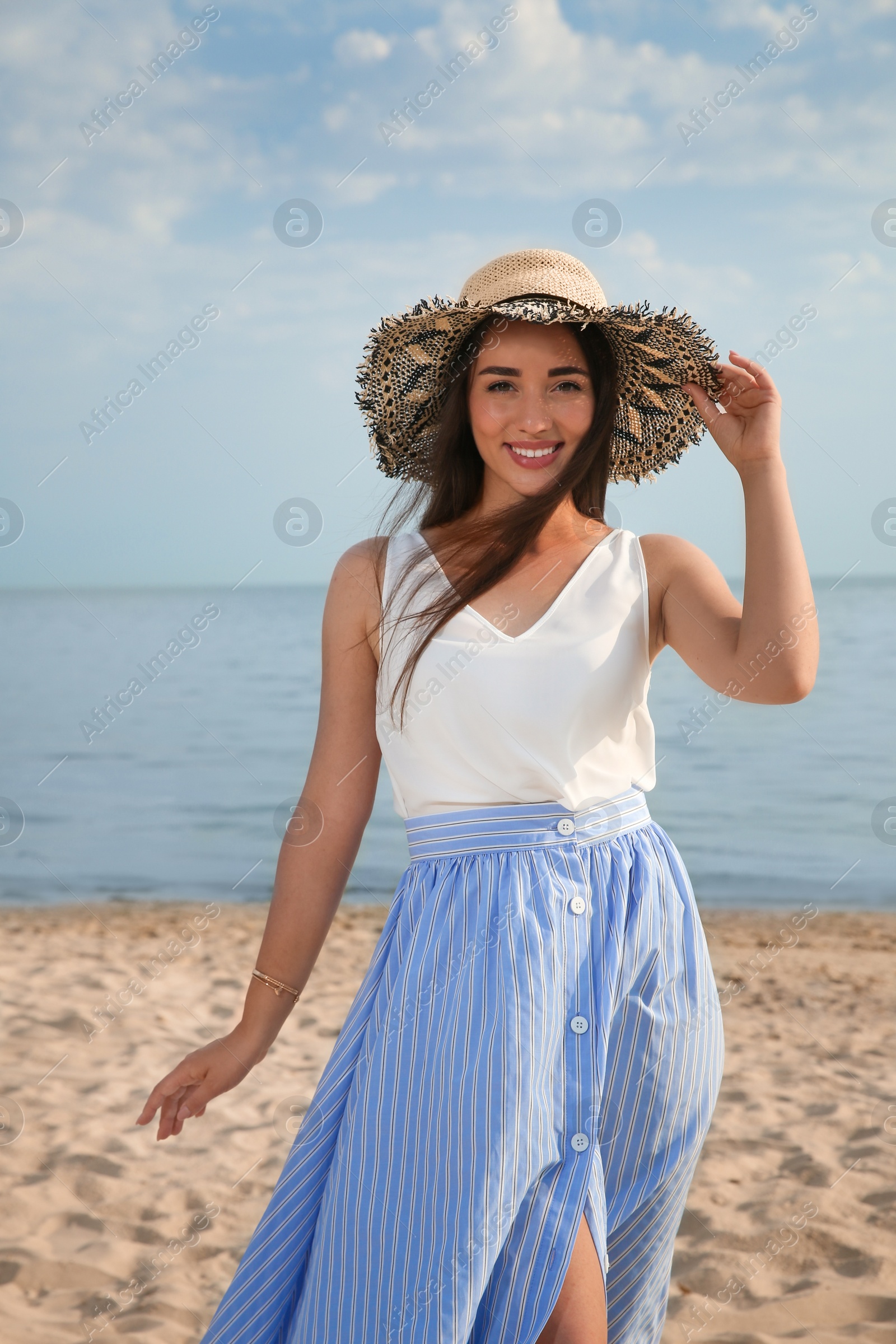 Photo of Beautiful young woman wearing straw hat on beach. Stylish headdress