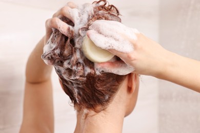 Young woman washing her hair with solid shampoo bar in shower, back view