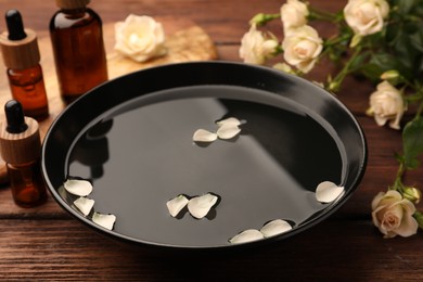 Bowl of water, bottles with essential oil and beautiful rose petals on wooden table. Aromatherapy treatment