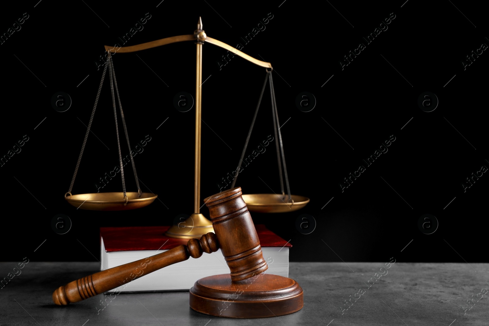 Photo of Judge's gavel, book and scales on grey table against black background, space for text. Criminal law concept