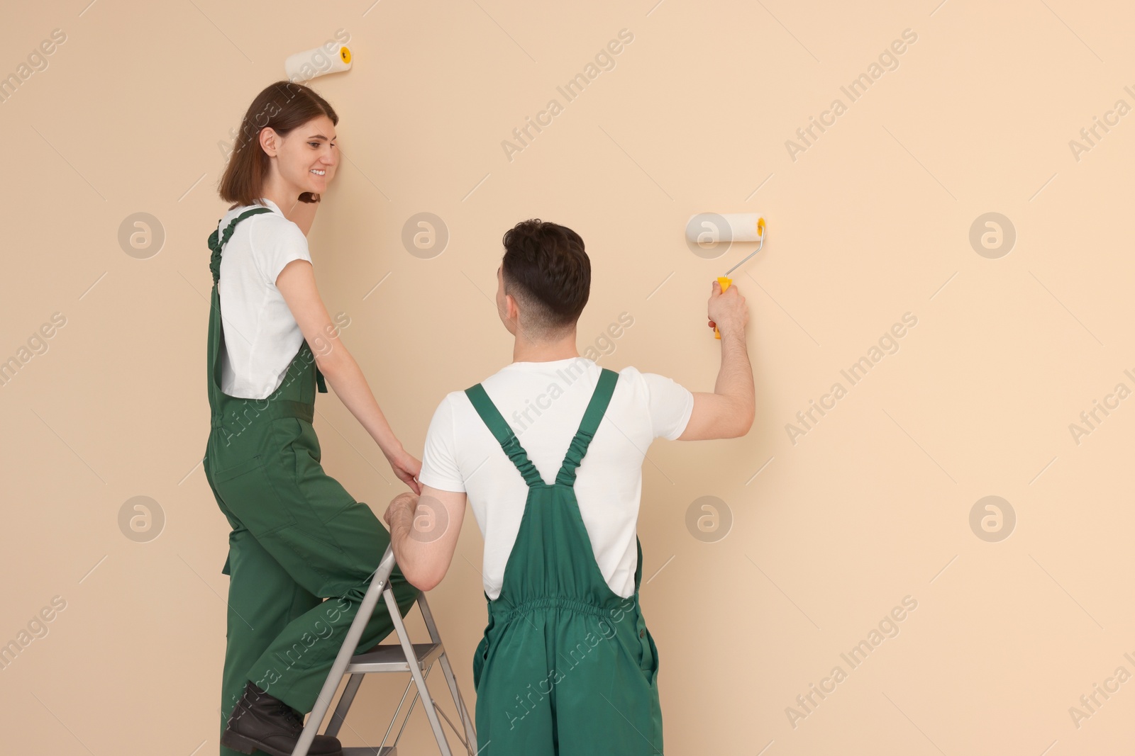 Photo of Young workers painting wall with rollers indoors. Room renovation