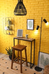 High wooden table with tablet and stool as stand up workplace near yellow brick wall. Stylish interior