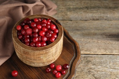 Cranberries in bowl on wooden table, space for text