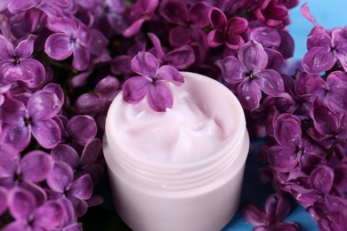 Jar of cream and lilac beautiful flowers as background, closeup