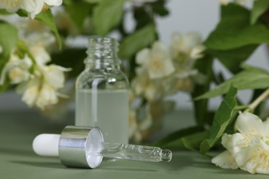 Photo of Essential oil in bottle, beautiful jasmine flowers and pipette on pale green background, closeup