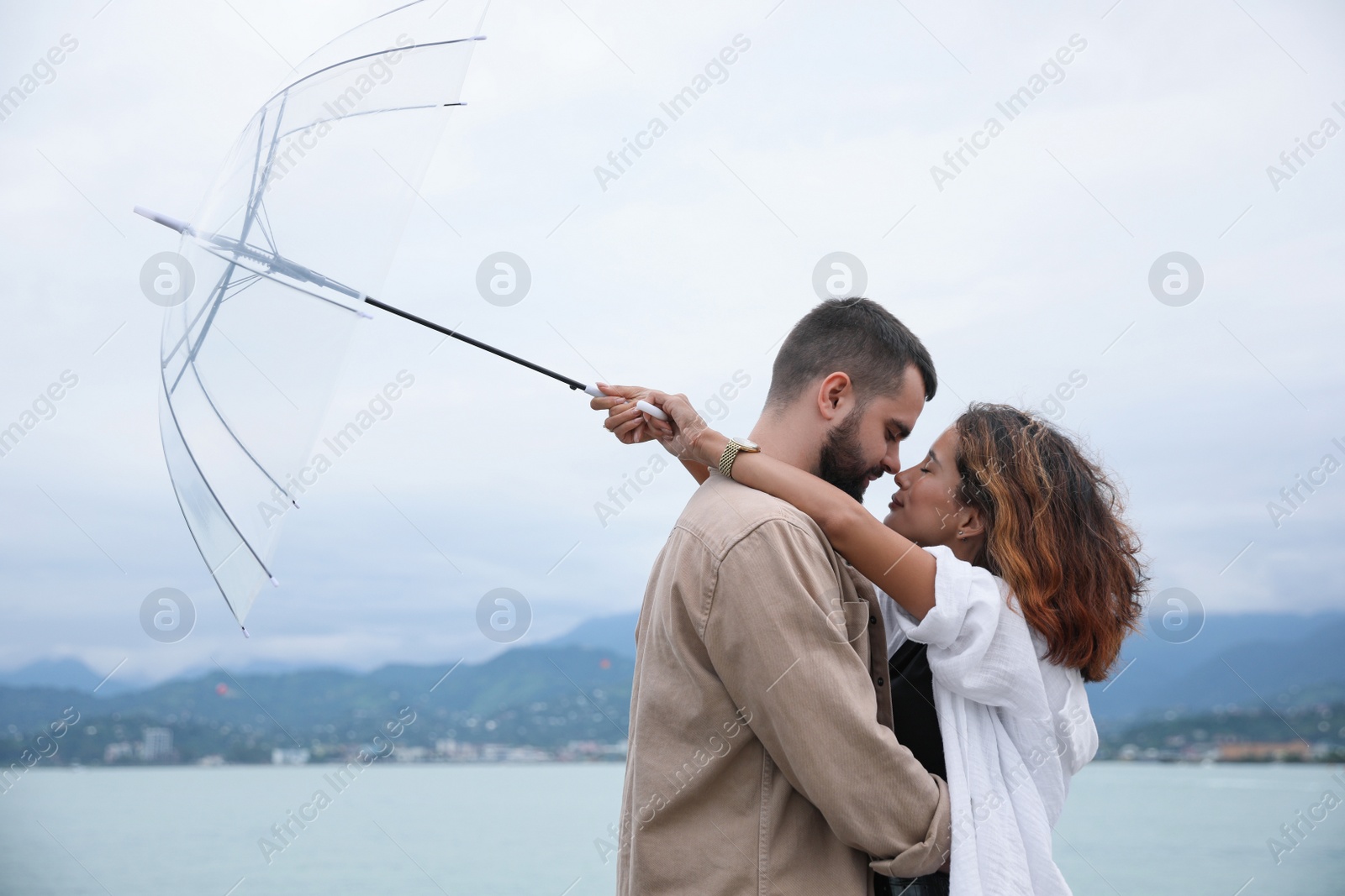 Photo of Young couple with umbrella enjoying time together under rain on beach, space for text