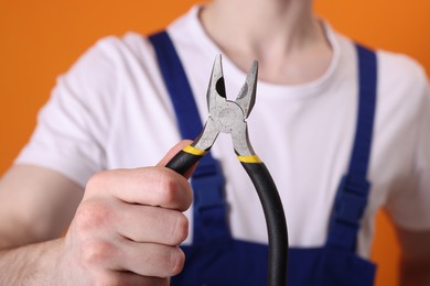 Photo of Young man holding pliers on orange background, closeup