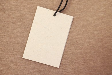 Photo of Cardboard tag on brown garment, top view. Space for text