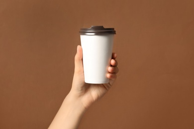 Woman holding takeaway paper coffee cup on brown background, closeup