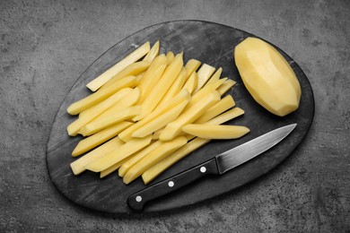 Photo of Whole and cut raw potatoes with knife on grey table, top view. Cooking delicious French fries