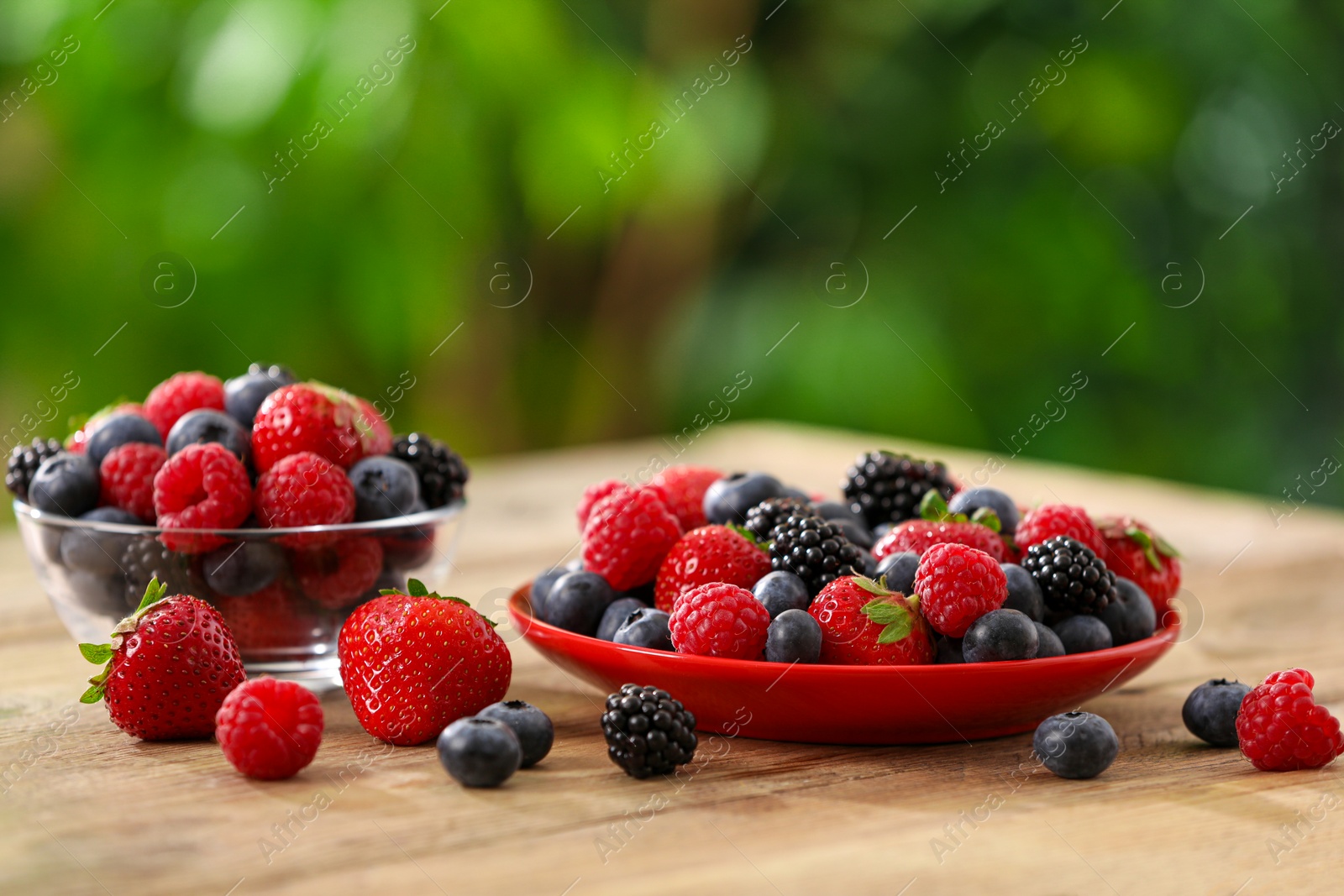 Photo of Different fresh ripe berries on wooden table outdoors