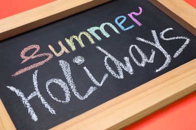 Photo of Chalkboard with phrase SUMMER HOLIDAYS on coral background, closeup. School's out