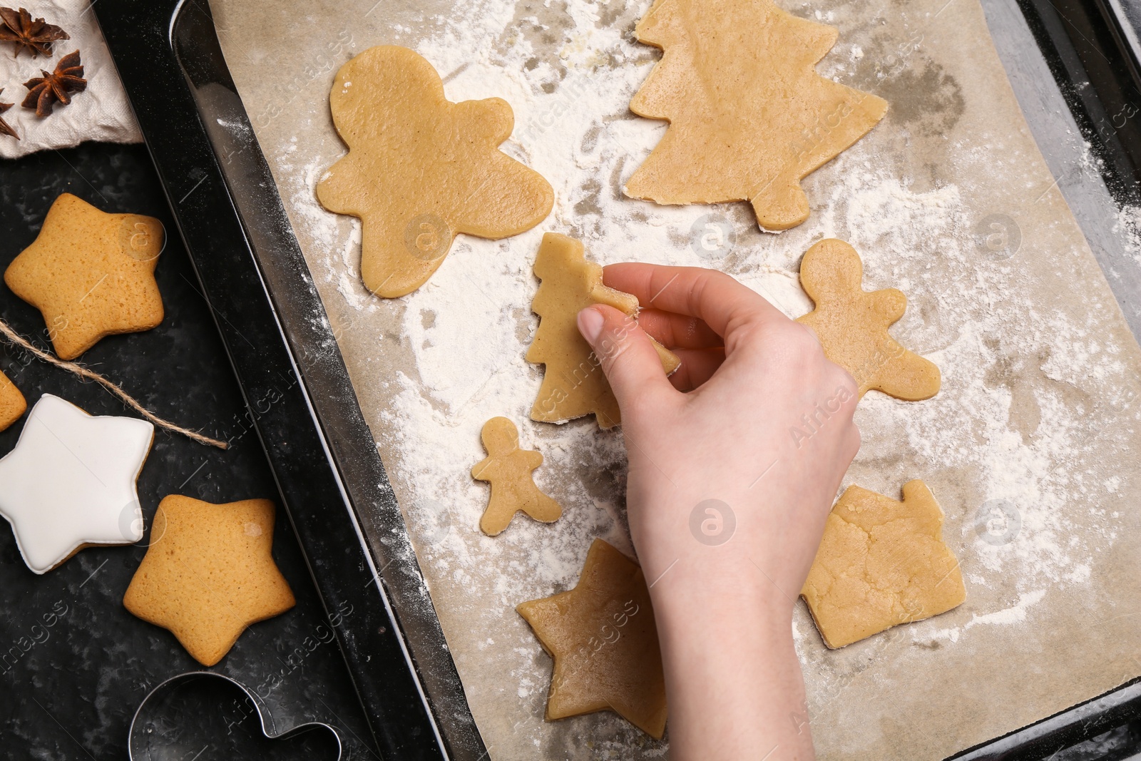 Photo of Woman putting raw Christmas cookies on baking tray at dark table, top view