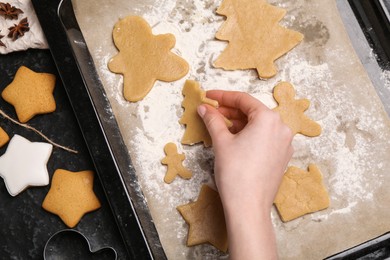 Photo of Woman putting raw Christmas cookies on baking tray at dark table, top view