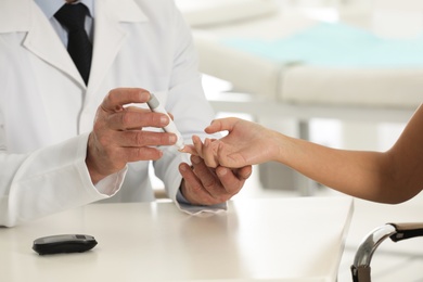 Photo of Doctor taking patient's blood sample with lancet pen in hospital, closeup. Diabetes control