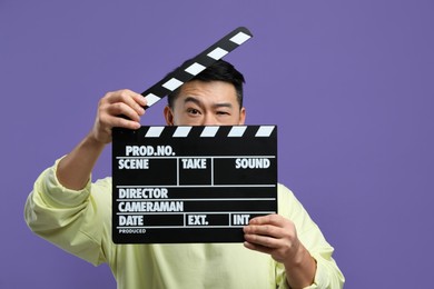 Photo of Asian actor with clapperboard on purple background. Film industry
