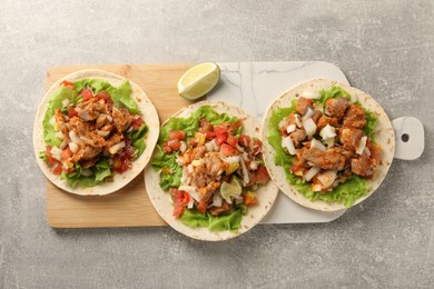Photo of Delicious tacos with vegetables, meat and lime on grey textured table, top view