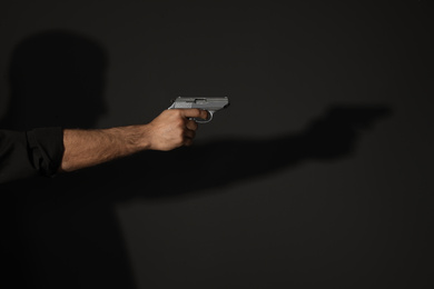 Photo of Professional killer with gun on black background, closeup