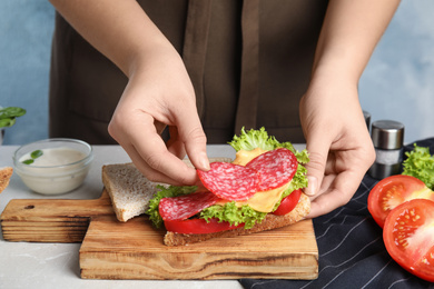 Photo of Woman making tasty sandwich with sausage at table, closeup