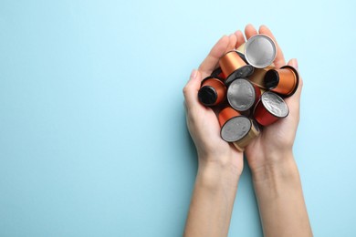 Photo of Woman holding heap of coffee capsules on light blue background, top view. Space for text