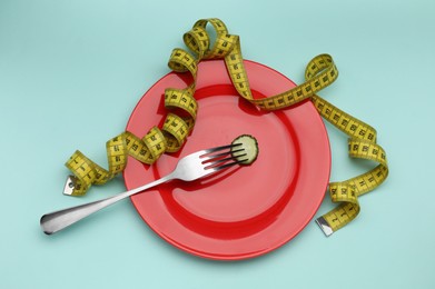 Photo of Plate with cucumber slice, measuring tape and fork on turquoise background, top view. Diet concept