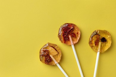 Photo of Sweet colorful lollipops with berries on yellow background, flat lay. Space for text