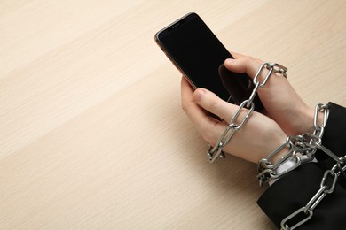 Photo of Man holding smartphone in chained hands at wooden table, above view. Internet addiction