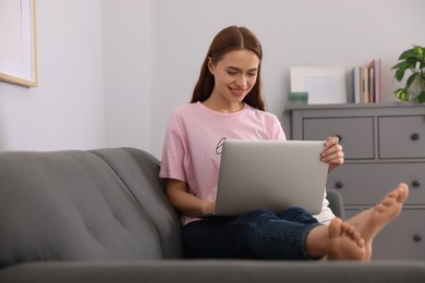 Photo of Happy young woman with laptop on sofa at home