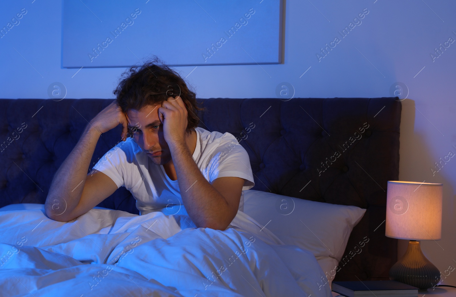 Photo of Handsome young man suffering from insomnia in dark room at night. Bedtime