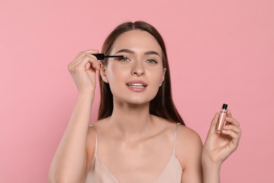 Photo of Young woman applying oil onto her eyelashes on pink background