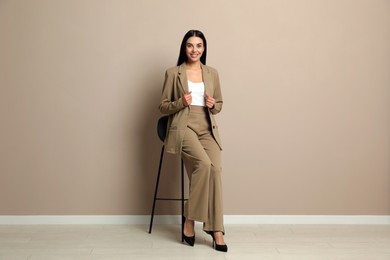 Photo of Beautiful young businesswoman sitting on stool near beige wall